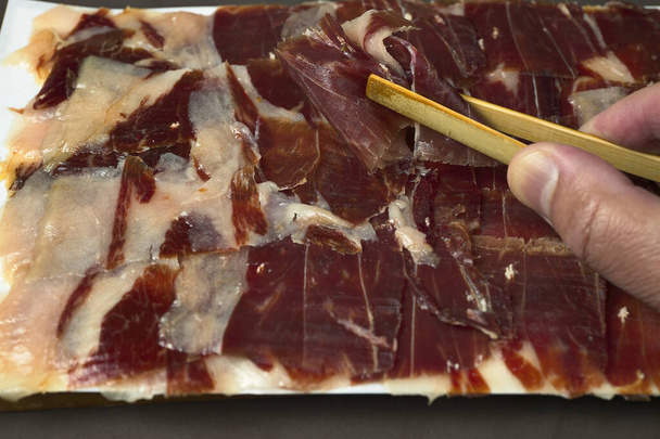 Iberian Ham. Man's hand, taking some wooden tongs and a plate of Iberian ham - Foto, Imagem