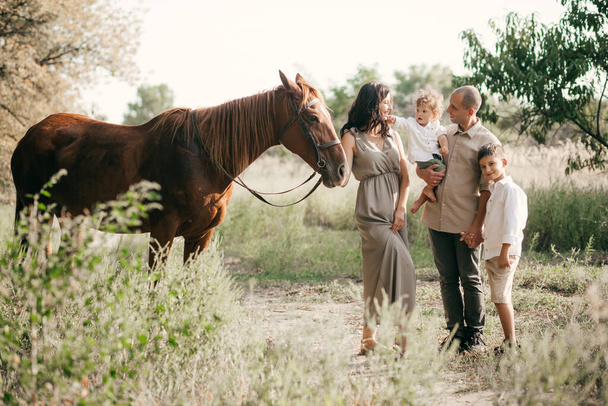 Счастливая молодая семья с двумя детьми на пшеничном летнем поле. Тур, путешествия, туризм, поход и люди - счастливая семейная прогулка - Фото, изображение
