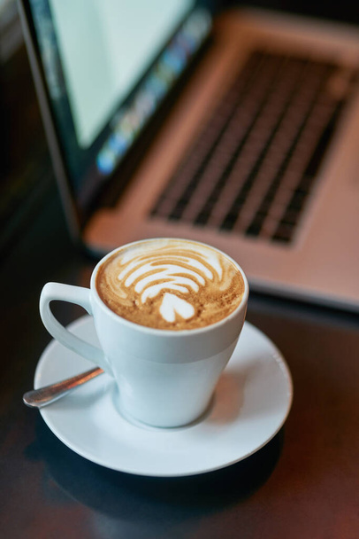 Freshly brewed to perfection. Still life shot of a cup of coffee and a laptop on a table. - Photo, image