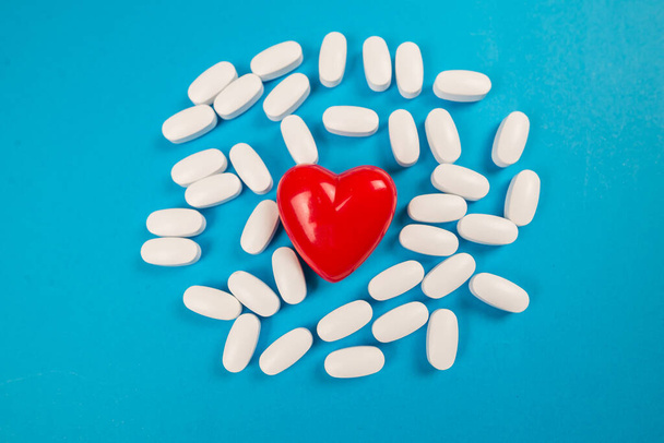 Kleine rote Herzen und weiße Pillen auf blauem Hintergrund. Medizinisches Konzept. - Foto, Bild
