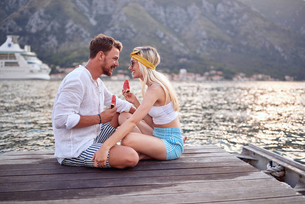 Romantic holiday.  couple sitting together on lake bank and enjoying eating watermelon - Фото, зображення