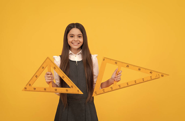 veselý dospívající dívka držet matematika trojúhelník pravítko ve škole na žlutém pozadí, vzdělání - Fotografie, Obrázek