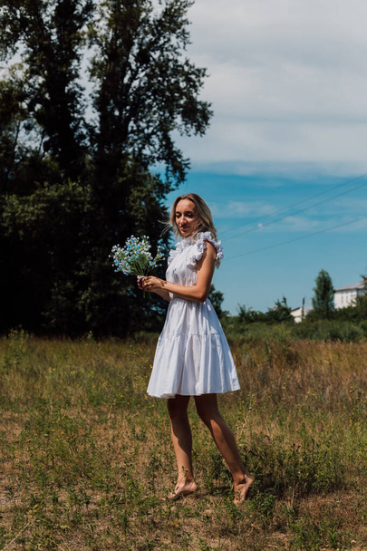 Una ragazza cammina attraverso un campo in campagna con i fiori in mano - Foto, immagini