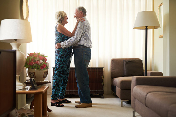 Lasting romance means always putting your best foot forward. Shot of a happy senior couple dancing together at home. - Фото, изображение
