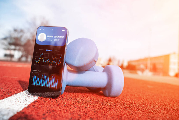 健康アプリ。フィットネス健康やダンベルの背景にスポーツジムのモバイルアプリケーションとスマートフォンの画面。ホームオンラインワークアウト - 写真・画像
