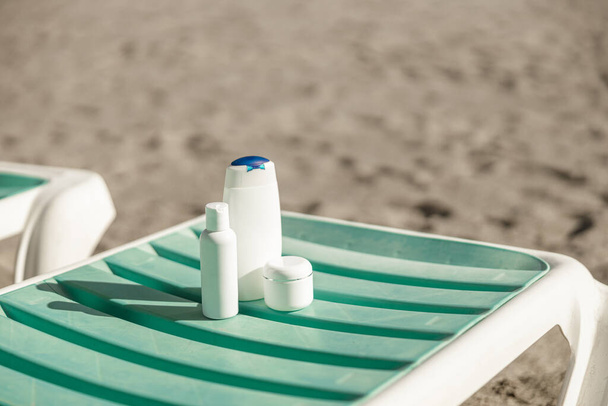 Suntan product bottles on the summer beach. Sunscreen on deck chair outdoors at beach resort - 写真・画像