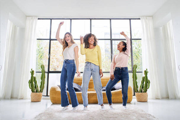Különböző női barátok táncolnak a nappaliban. Multiracionális boldog nők játszanak és ünneplik az élet örömét Vidám lányok élvezik együtt otthon szórakozás.  - Fotó, kép