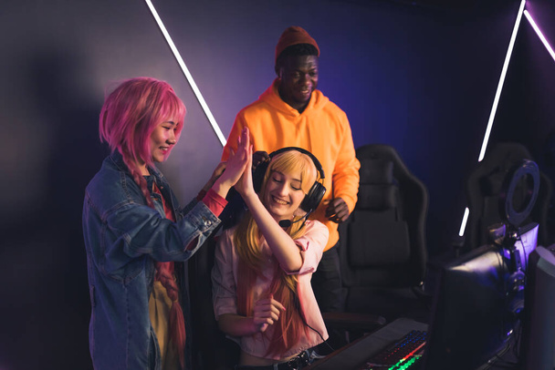 High five. Young female beginner gamer is happy after her first win. Teammates supporting their friend in gaming cafe. - Foto, Imagem