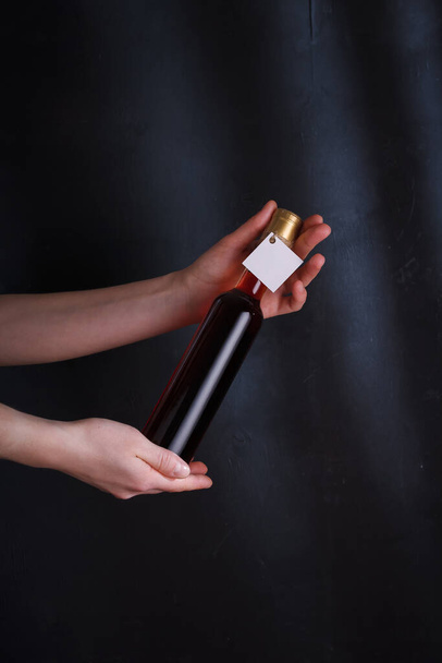 weibliche Hände, die 250 ml Flasche Rotwein mit Etikett-Attrappe halten, keine Marke auf schwarzem Hintergrund. Alkohol trinken, Raum kopieren - Foto, Bild