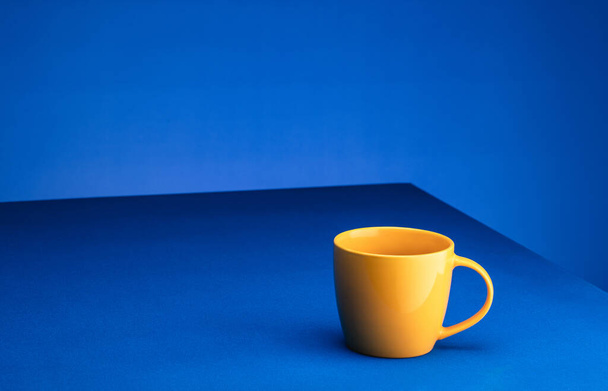 Yellow coffee cup stands on a blue table against a blue background. The concept of minimalism. Place for text - Foto, imagen