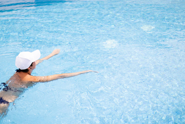 Fiatal nő fehér sapkában úszás egy medencében kék tiszta vízzel. - Fotó, kép