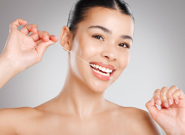 Clean teeth are happy teeth. Studio shot of an attractive young woman flossing her teeth against a grey background. - Φωτογραφία, εικόνα