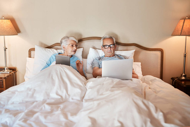 Imparare a utilizzare la tecnologia nel XXI secolo. Colpo ritagliato di una coppia di anziani seduti a letto insieme e utilizzando la tecnologia in una casa di cura. - Foto, immagini