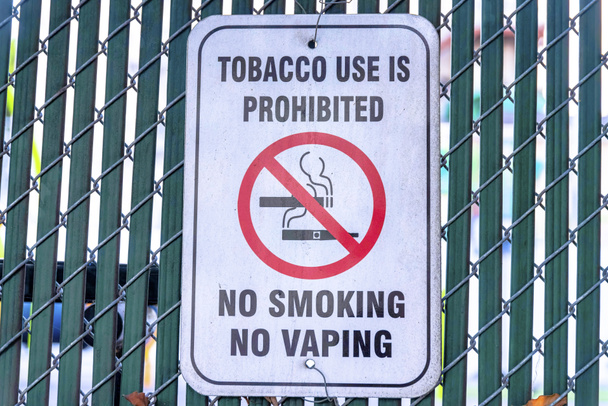 El consumo de tabaco está prohibido no fumar no hay señales de vapeo en San Francisco, California. Primer plano de una señalización de no fumar en una valla de malla metálica con listones de privacidad. - Foto, imagen