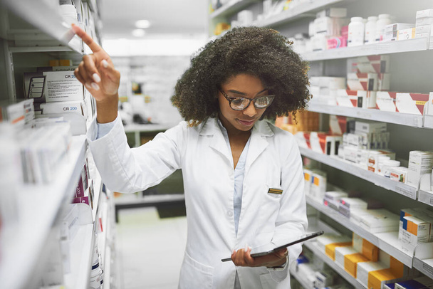 This is in the right place. Shot of a cheerful young female pharmacist checking stock on the shelves of a pharmacy. - Foto, afbeelding