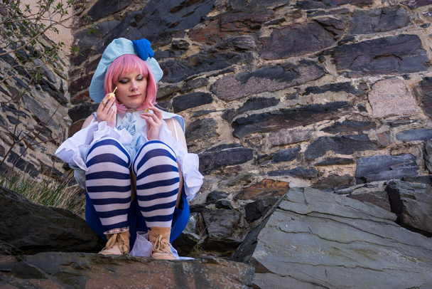 a beautiful woman dressed up as an anime character sits on a rock - Foto, afbeelding