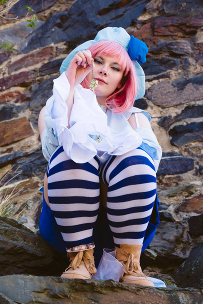 a beautiful woman dressed up as an anime character sits on a rock with a key in the hand - Foto, Bild