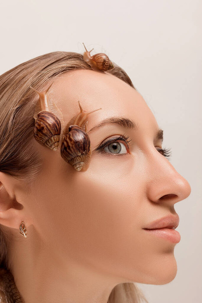 Petits et grands escargots d'achatines rampent sur le visage et le cou d'une jeune fille - Photo, image