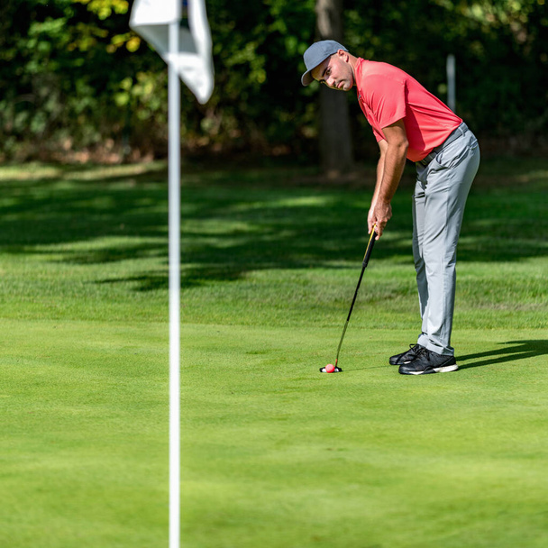 Golfeur dans la chemise rouge sur le vert, mettre vers le drapeau de golf - Photo, image