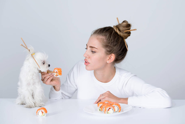 Japanese sushi style. Fashion portrait of beauty model girl eating sushi rolls, japanese food. Beautiful woman holding chopsticks with sushi. Sexy lady with pet dog advertisement. - Фото, изображение