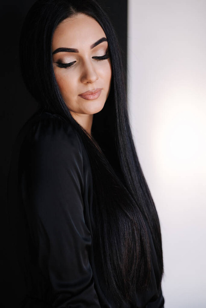 Portrait of gorgeous female in black dress. Brunette woman close her eyes to show make up. Studio photo shoot - Foto, Imagen