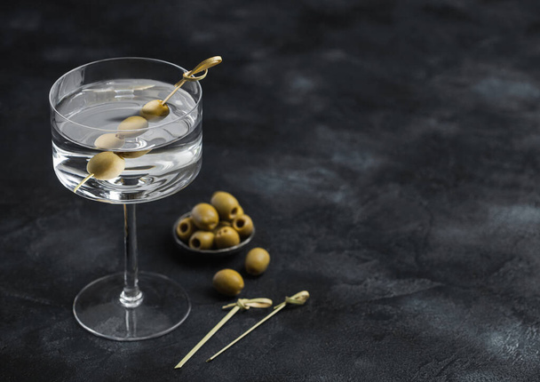 Vodka martini gin cocktail in modern glass with olives in metal bowl and bamboo sticks on black background.Top view - Fotografie, Obrázek