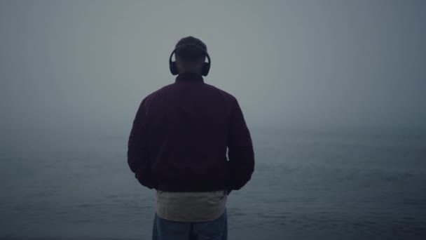 Ο άνθρωπος ακούει μουσική ακουστικά στη θάλασσα παραλία. Ο τύπος απολαμβάνει τη μουσική στα ακουστικά - Πλάνα, βίντεο