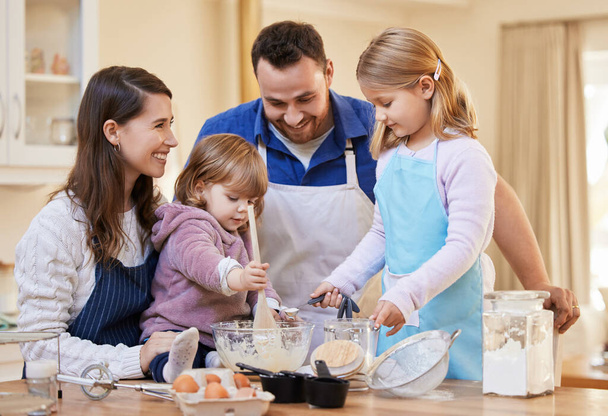 El tiempo en familia es todo lo que importa. Tiro de una familia horneando juntos mientras una niña revuelve un tazón de masa de pastel. - Foto, imagen