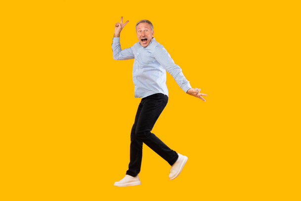 Excited mature man jumping up at yellow orange studio - Photo, Image