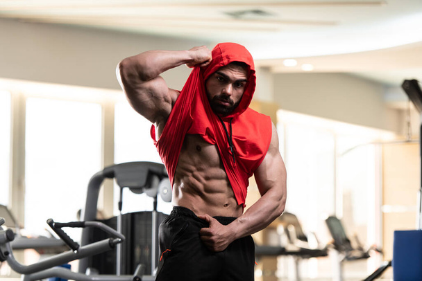 Young Man Standing Strong In The Gym And Flexing Muscles in a Red Hoodie  - Muscular Athletic Bodybuilder Fitness Model Posing After Exercises - Foto, Imagem