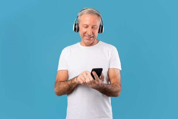 Dojrzały mężczyzna korzystający z telefonu komórkowego w słuchawkach bezprzewodowych - Zdjęcie, obraz