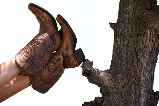 Випадковий ковбой. Обрізаний знімок людини в ковбойських черевиках, що спираються на дерево
. - Фото, зображення