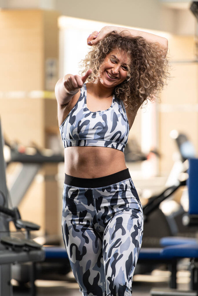 Attractive Young Woman Showing Thumbs Up While Standing Strong In The Gym And Flexing Muscles - Beautiful Athletic Fitness Model Posing After Exercises - 写真・画像