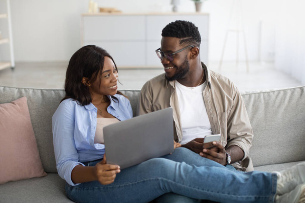 Happy black couple sitting on couch, using smartphone and pc - Photo, Image