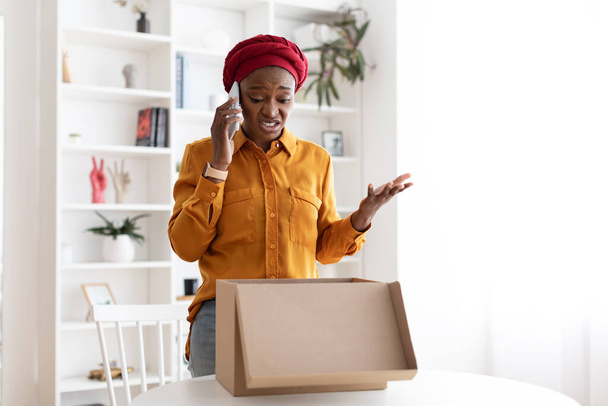 Enfadado comprador negro señora mirando dentro de la caja de entrega y llamando - Foto, Imagen