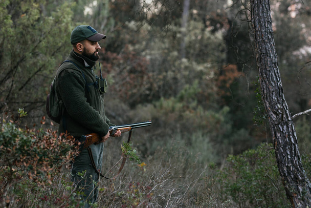 Junger Jäger hält mitten in der Natur sein Gewehr in der Hand und blickt nach unten - Foto, Bild