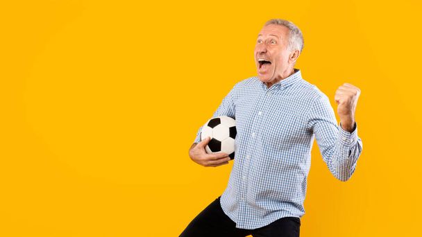 Hombre maduro gritando sosteniendo pelota de fútbol sobre fondo amarillo - Foto, imagen