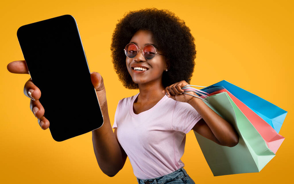 Стильная молодая черная женщина с покупками и мобильным телефоном - Фото, изображение