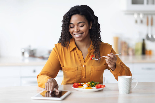 Csinos afro-amerikai nő reggelizik, digitális tabletta, mockup - Fotó, kép