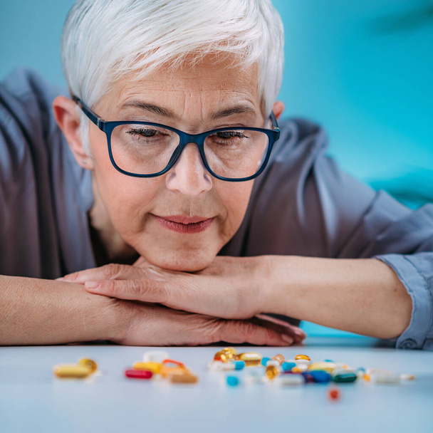 Prescribed medication non-adherence. Senior female patient counting pills.  - Foto, Bild