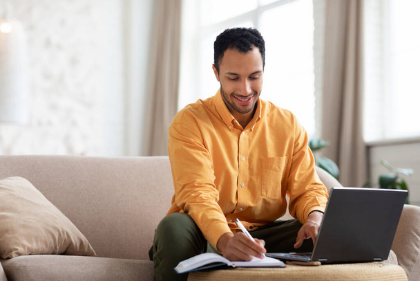 Portrait of smiling Arab man using laptop and writing - Photo, image