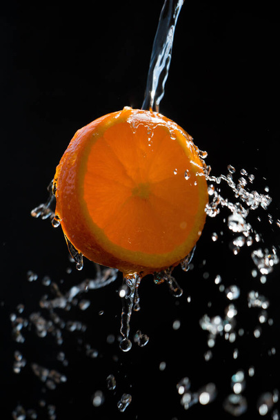 Una rebanada de naranja se rocía con abundante agua sobre un fondo negro - Foto, Imagen