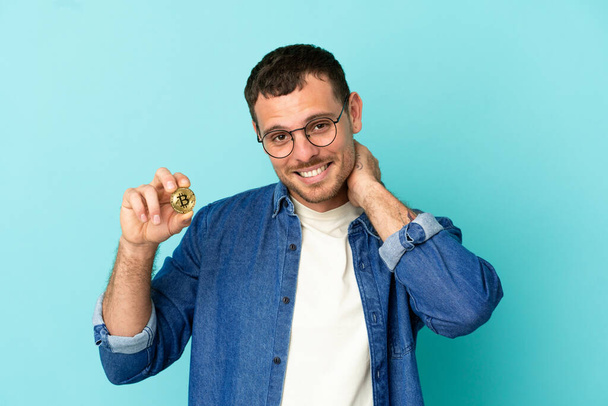 Brazilian man holding a Bitcoin over isolated blue background laughing - 写真・画像