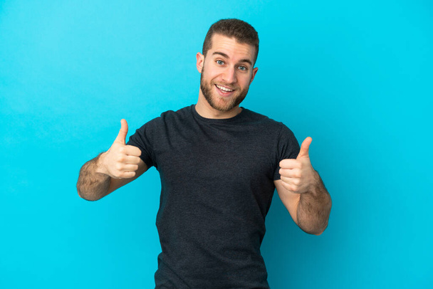 Young handsome caucasian man isolated on blue background giving a thumbs up gesture - Φωτογραφία, εικόνα