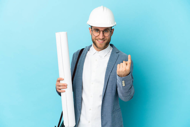 Mladý architekt muž s helmou a drží plány na izolovaném pozadí dělá nadcházející gesto - Fotografie, Obrázek