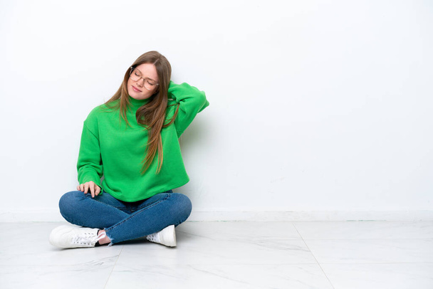 Mladá běloška žena sedí na podlaze izolované na bílém pozadí s bolestí krku - Fotografie, Obrázek