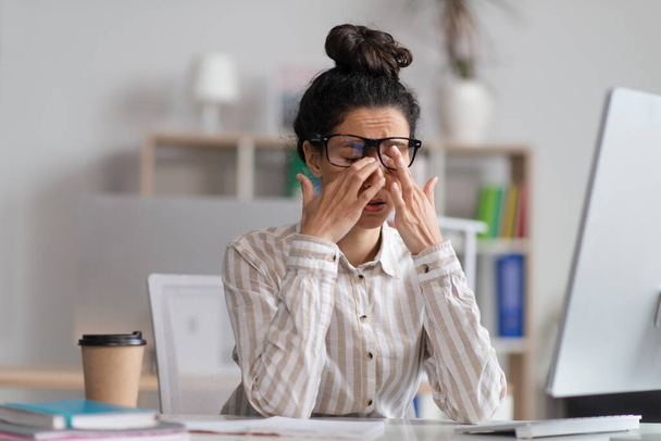Női irodai dolgozó szemüvegben dörzsöli fáradt szemét, kimerült a túlmunka, ül a munkahelyen az irodában - Fotó, kép