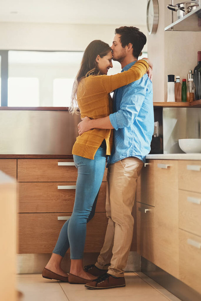 Sealed with a kiss. Shot of an affectionate young man kissing his girlfriend on the forehead in their kitchen. - Foto, afbeelding