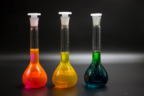 Close-up picture of colorful liquids in the volumetric flask. Chemical substances, and solutions in the black background. The colorful solutions line up in black background.  - Фото, изображение