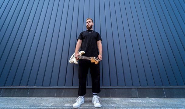 Young street musician playing guitar near the big blue wall - Φωτογραφία, εικόνα